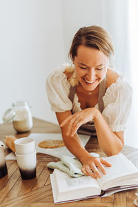 Smiling woman reading a recipe book while cooking at kitchen