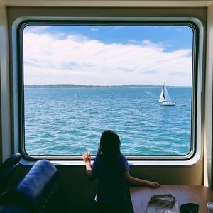 Rear view of girl looking at sea through window