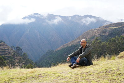 Full length portrait of mid adult man sitting against mountains