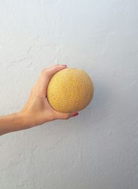 Cropped hand holding muskmelon against white wall