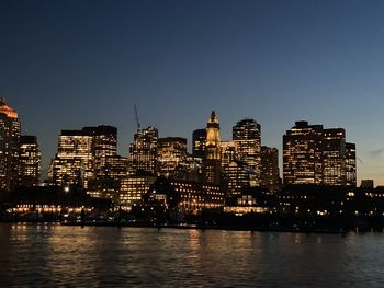 Illuminated buildings by river against sky in city