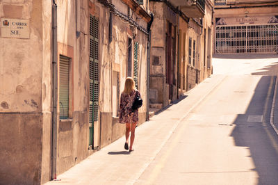 Rear view of woman walking on street amidst buildings in city