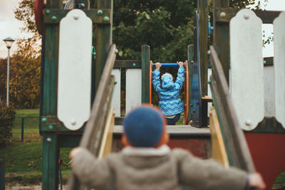 Rear view of boy and girl on playground equipment