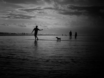 Silhouette people on beach against sky during sunset