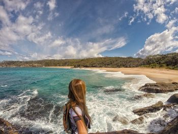 Rear view of boy standing in sea against sky