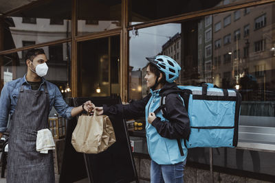 Male owner giving order to delivery woman outside deli store during pandemic