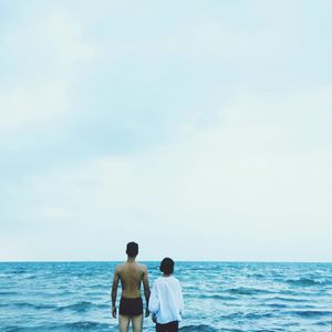 Rear view of couple standing by sea against clear sky