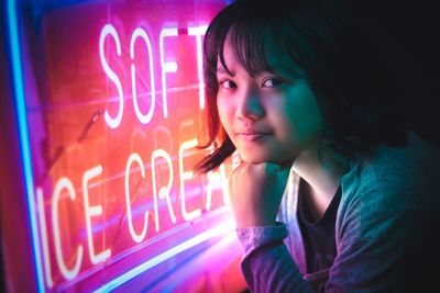 Close-up portrait of woman by illuminated neon sign