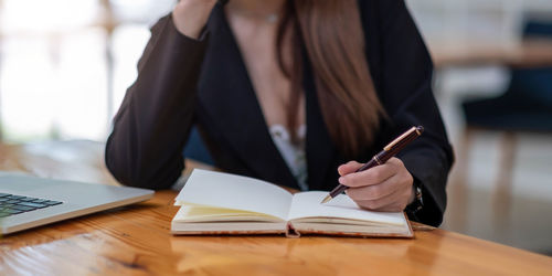 Midsection of woman reading book while sitting on table