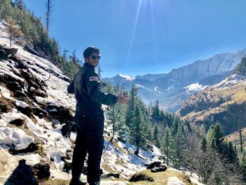 Young man wearing sunglasses while standing on mountain against blue sky during sunny day