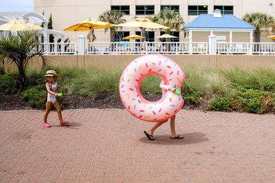 Two girls walking to pool with oversized donut raft wearing hat