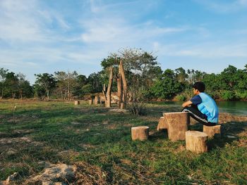 Rear view of man sitting on field against sky