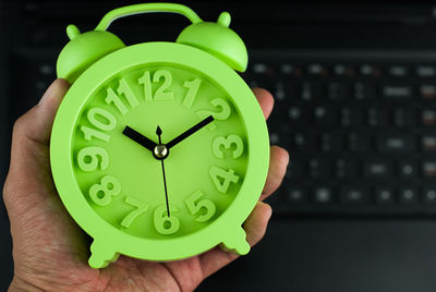 Cropped hand holding green alarm clock at home