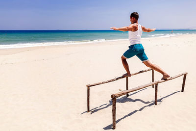 Side view of man balancing on beams on beach