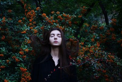 Portrait of beautiful young woman standing by leaves in forest