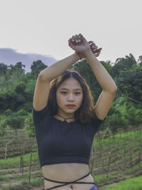 Portrait of young woman with arms raised standing outdoors