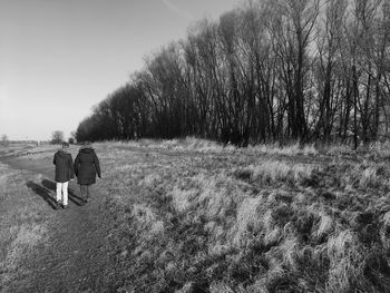 Rear view of mother and son walking on field