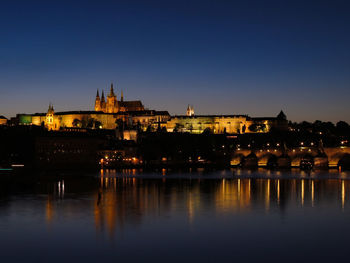 Illuminated buildings by river against sky in city