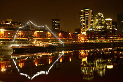 Illuminated buildings by river against sky at night