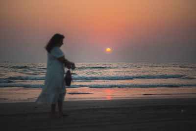 Silhouette woman standing at beach during sunset