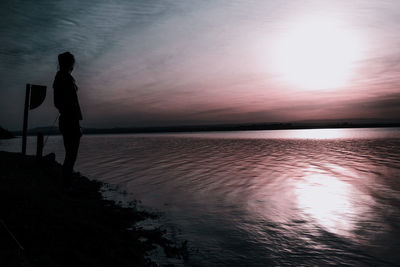 Silhouette man standing by sea against sky during sunset