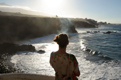 Rear view of woman standing at beach against sky