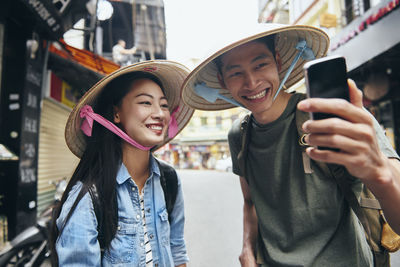 Portrait of smiling young couple wearing hat taking selfie at market
