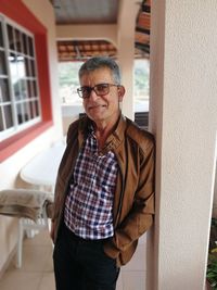 Portrait of senior man standing on porch by house