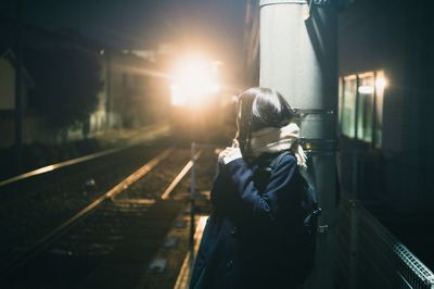 Woman standing on railroad station platform at night