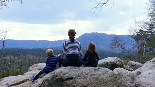 Rear view of people sitting on rock against sky