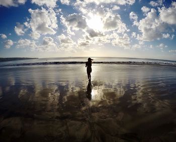 Rear view of silhouette young woman standing at beach against cloudy sky during sunset