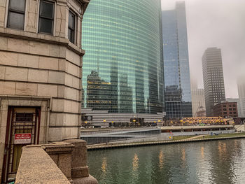 Modern buildings by river in city against sky