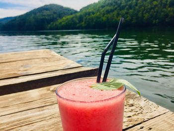 Glass of strawberry lemonade with mint placed on wooden pontoon near the lake