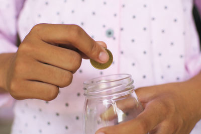 Midsection of person inserting coin in jar