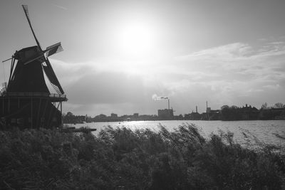 Traditional windmill on field by river against sky