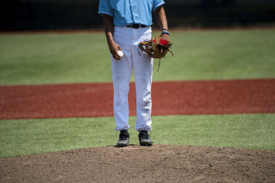 Low section of baseball player standing on playing field during sunny day