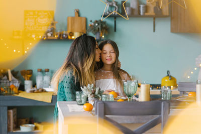 Mom kisses her daughter on the cheek at the festive christmas table