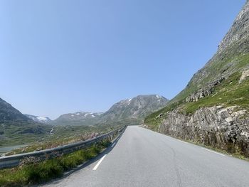 Empty road amidst mountains against clear blue sky