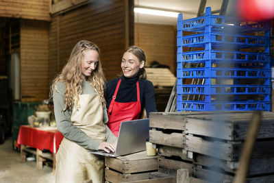 Two happy women using laptop between crates on a farm