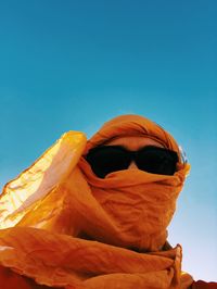 Low angle view of woman wearing sunglasses against clear blue sky