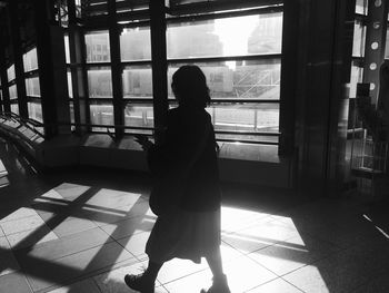 Rear view of woman walking on floor against window
