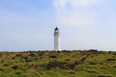 Lighthouse on field by building against sky