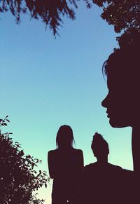 Low angle view of silhouette mother and trees against clear blue sky