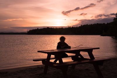 Silhouette person sitting on beach against sky during sunset