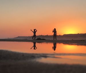 Silhouette woman in bikini standing at beach against sky during sunset