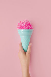 Cropped hand of person holding ice cram against pink background