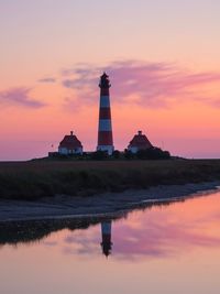 Lighthouse by sea against sky during sunset