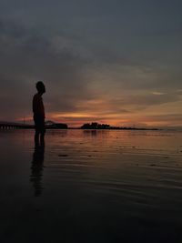 Silhouette man standing in sea against sky during sunset