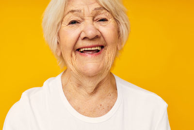 Portrait of smiling senior woman against yellow background