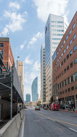 Road by buildings against sky in city